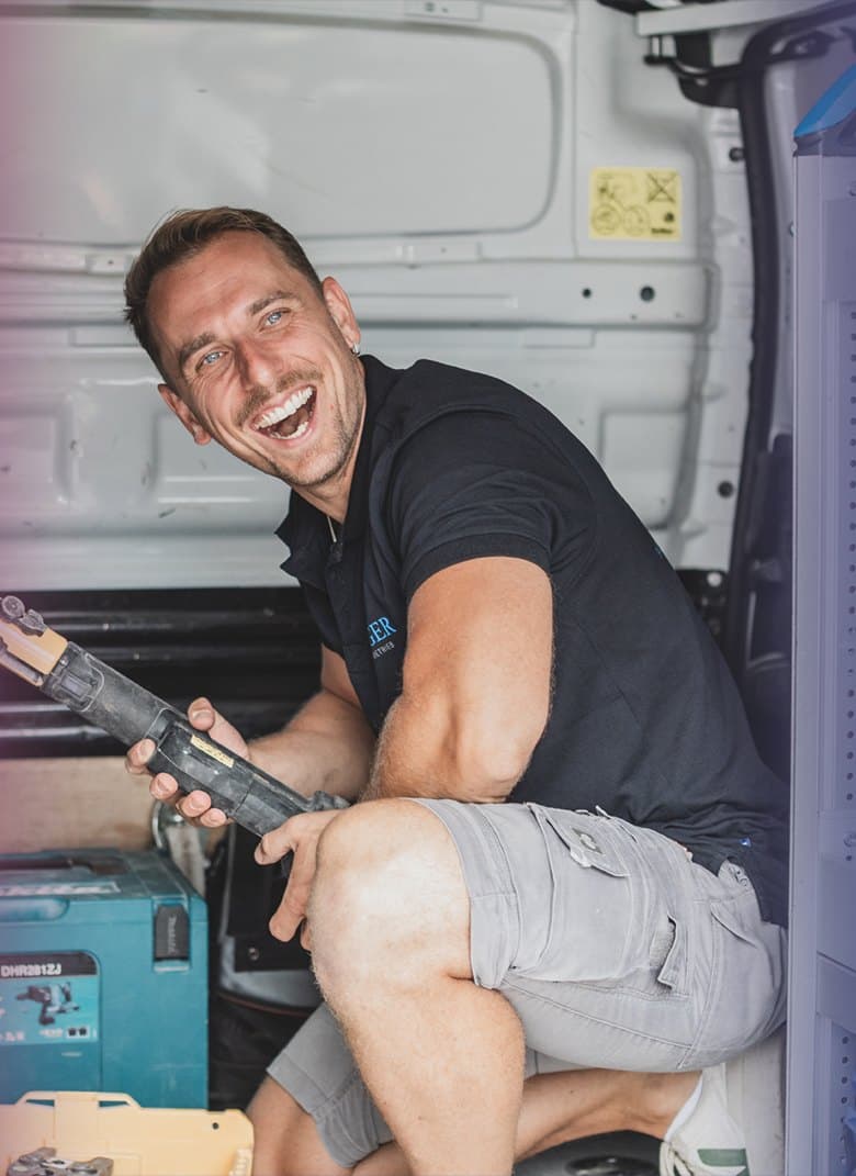 Monteur von Senger Haustechnik lacht im Firmentransporter, Werkzeug in der Hand